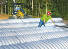Operator Larry Dillon runs a front-end loader equipped with forks, as Laborer Wes Winebrimmer readies drainage pipe for loading. (Photo by Carl Thiemann)