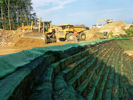 A haul truck brings in more fill as Dozer Operator Larry Griffith spreads the material, while David McGuire and Roller Operator Evelyn Jarrell compact it, in an area of Vecellio & Grogan's East Beckley Bypass job known as the wall project. A wire mesh- and geo-fabric-reinforced retaining system provides the needed slope and stability as the area is brought up to grade one layer at a time. Grass seed in each shelf puts the finishing touches on the wall. (Photo by Carl Thiemann)