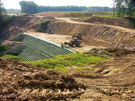 A loader brings fill to crew members with shovels along the edge of the tiered wall project. (Photo by Carl Thiemann)