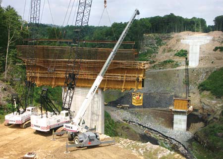 A crew of steel workers is lifted out to a bridge pier as Crane Operators Tommy Coiner and Richard Clary hold a rebar cage ready for placement on Vecellio & Grogan's East Beckley Bypass project. The crew will guide the cage into a waiting form, into which concrete will be poured to form a pier cap. (Photo by Carl Thiemann)