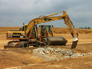 V&G Foreman Gus Rivero-Meneses, operating a rubber tire excavator with swivel bucket, works with Loader Operator J.P. Evans to shape a swale along a perimeter road.