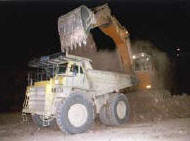 an excavator loads a dump truck at night
