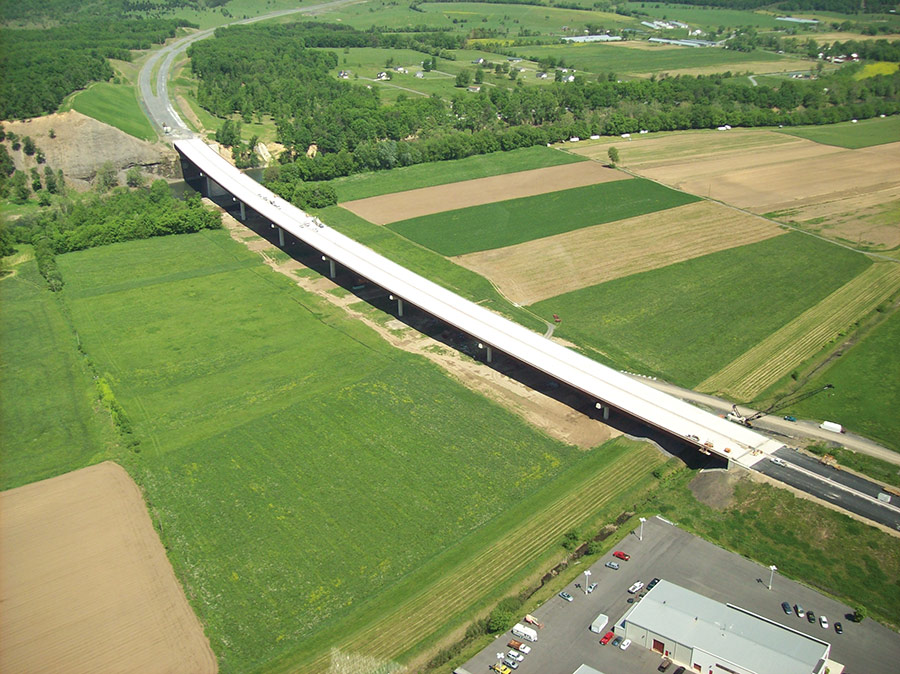 aerial view of a construction site of a long multi-lane bridge bordered by fields