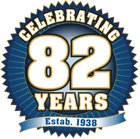 Over 8 Decades of Service decorative badge, circular with pointed outline. Text on badge says "Celebrating 82 years", Ribbon on badge says "Estab. 1938"